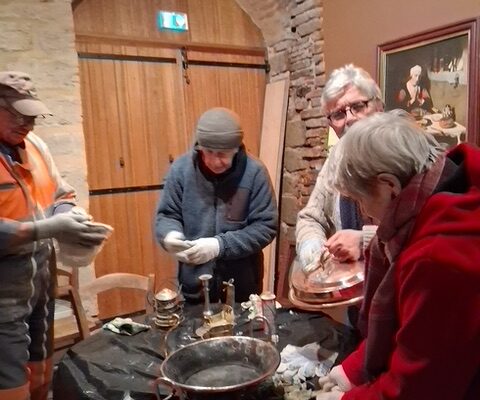 Quatre bénévoles nettoient des cuivres anciens autour d’une table