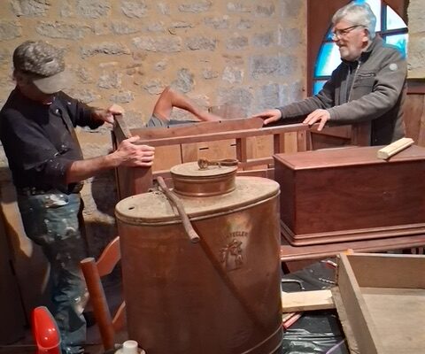 Deux bénévoles installent un lit ancien en bois dans le musée