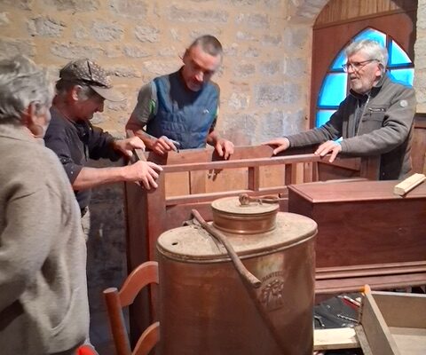 Quatre bénévoles assemblent un meuble ancien près d’une sulfateuse en cuivre