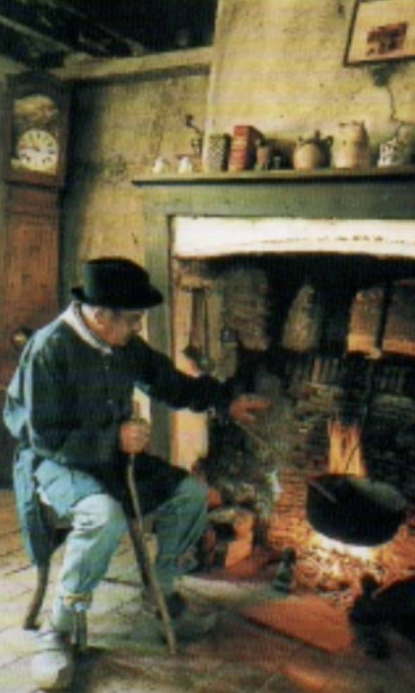 Un homme âgé en habit traditionnel attise le feu dans une grande cheminée quercinoise